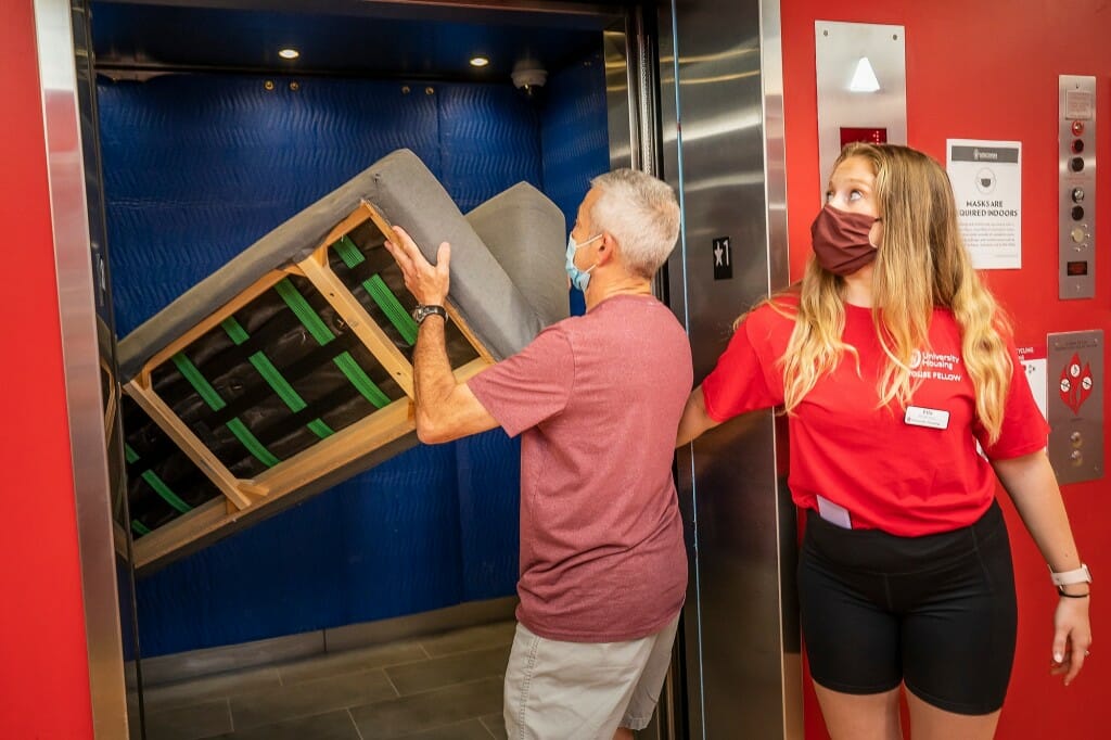 A man trying to fit a couch or futon into an elevator