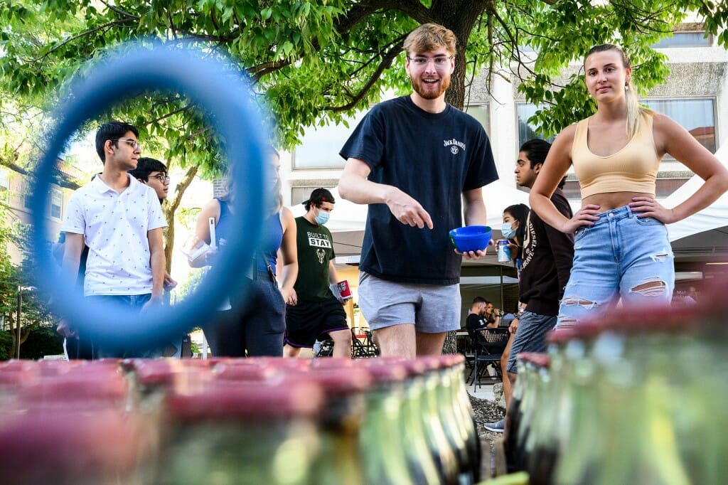 A student tossing a ring at some bottles while another student watches