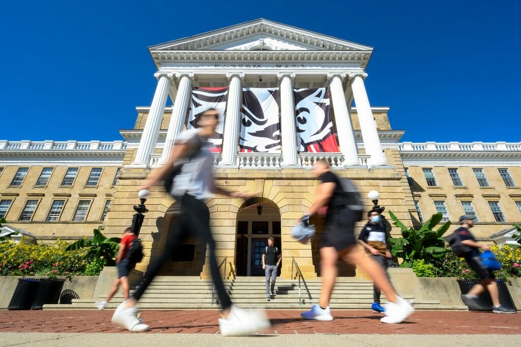 Several students walking quickly past Bascom Hall under a banner of a scowling Bucky Badger