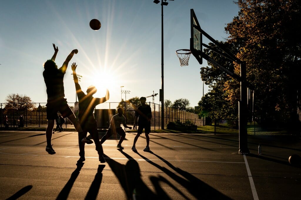 Several basketball players silhouetted against the setting sun
