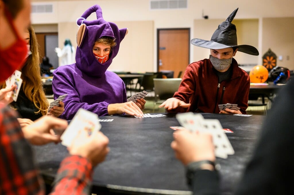 Two people in Halloween costumes and face coverings playing cards at a table