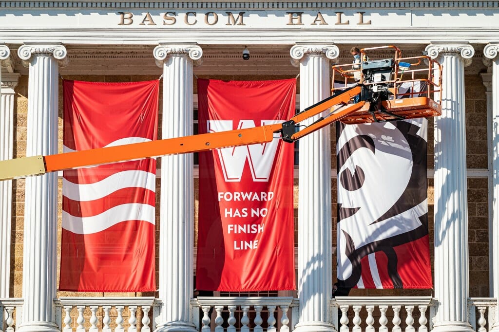 A 3-section banner between Bascom Hall's columns -- 2 panels of All Ways Forward coming down, one panel of Bucky going up