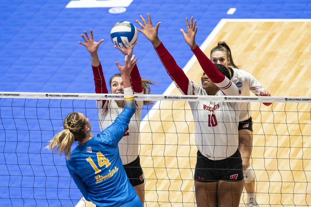 Two Wisconsin players raise their arms while a UCLA player hits the ball