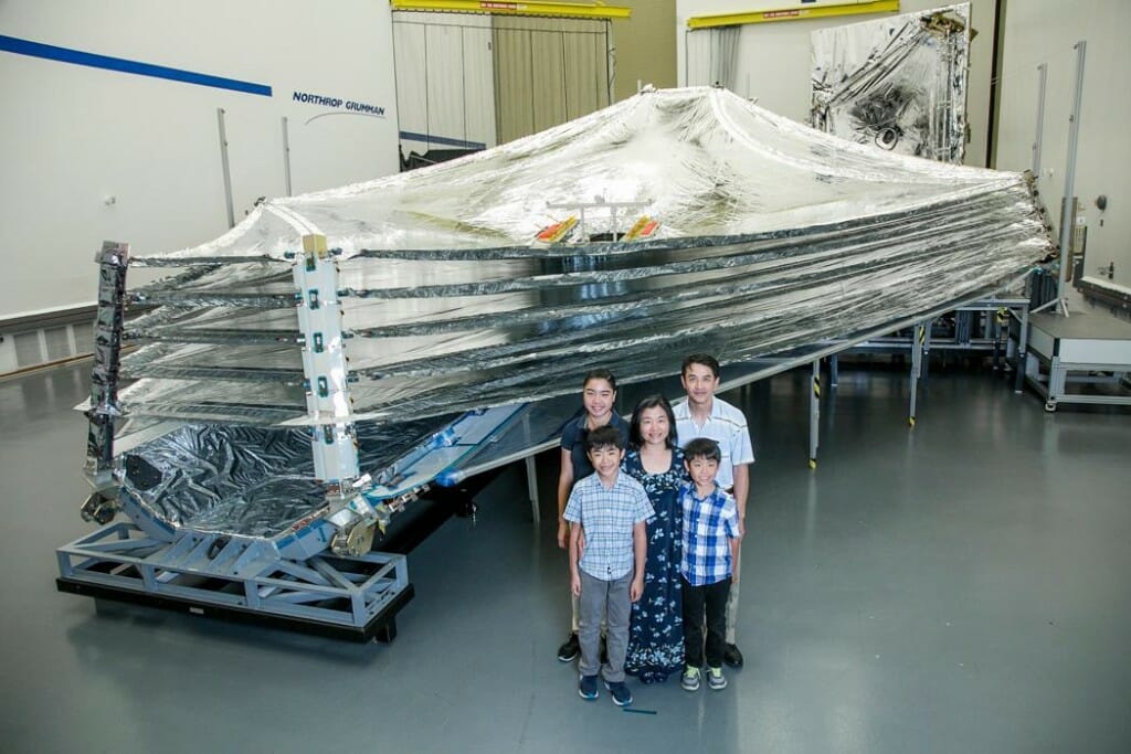 People standing in front of a large piece of space telescope equipment