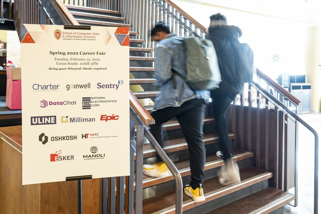 Students walk past a sign promoting a School of Computer, Data and Information Sciences career fair held in Varsity Hall inside Union South.