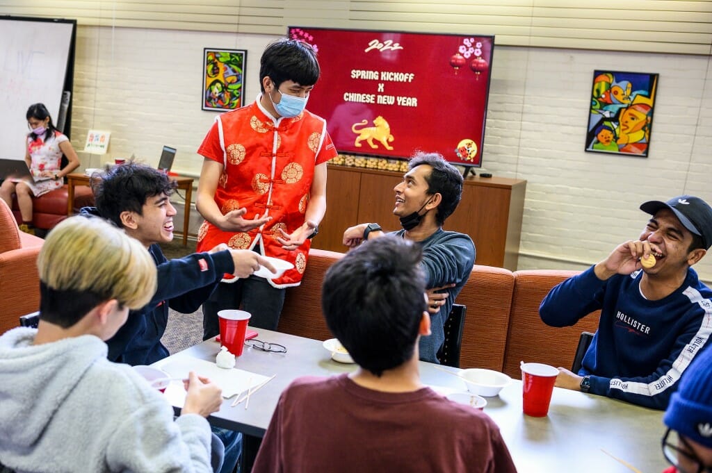 Standing and wearing a traditional Tang suit, Gan Zhao Yang, president of the Malaysian Student Association, talks with guests enjoying snacks.