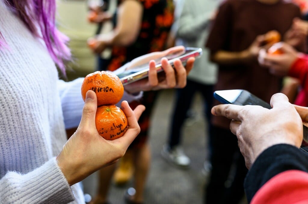 Photo: The hands of two people holding mandarin oranges and cell phones.