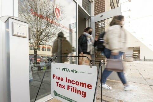 2 people walking out of the office's entrance past a sign that says "Free Income Tax Filing"