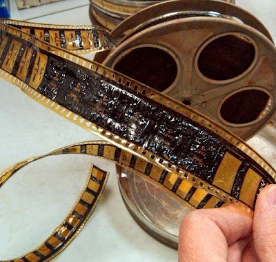 Closeup of a person's fingers holding a yellowed and crinkled piece of film from a film spool