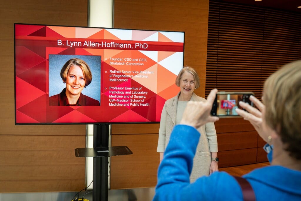Allen-Hoffman posing for a photograph in front of a slide of her portrait and bio projected on a video screen