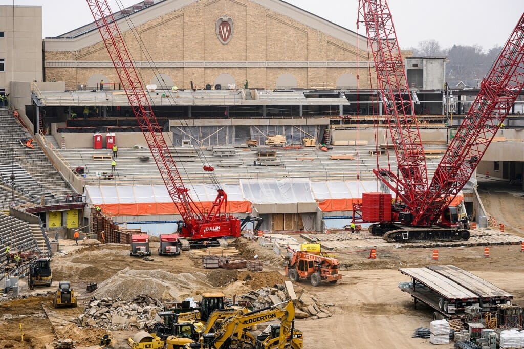 Construction equipment, including cranes and earth-movers, inside the stadium with the Field House behind