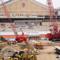Construction equipment, including cranes and earth-movers, inside the stadium with the Field House behind