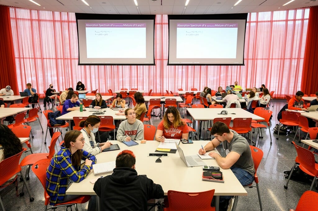 Students sitting at tables beneath projection screens