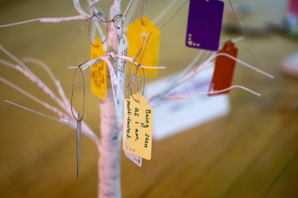 Tags with written responses to the prompted question “What does courage in community mean to you?” hang from decorative tree.