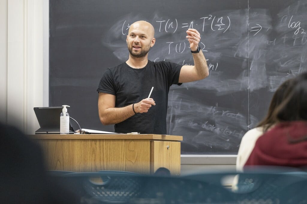 Aws Albarghouthi in a classroom, gesturing while standing at a lectern in front of a blackboard