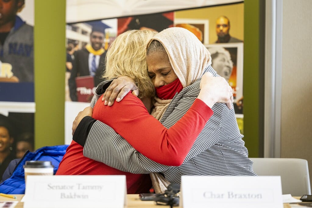 Baldwin and Braxton hugging while sitting behind a table