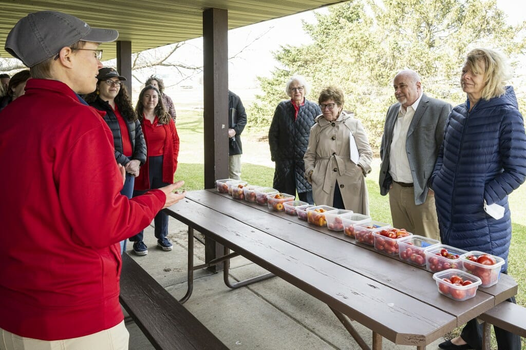 A person on one side of a folding table under an outdoor enclosure speaking to four people standing on the other side of the table