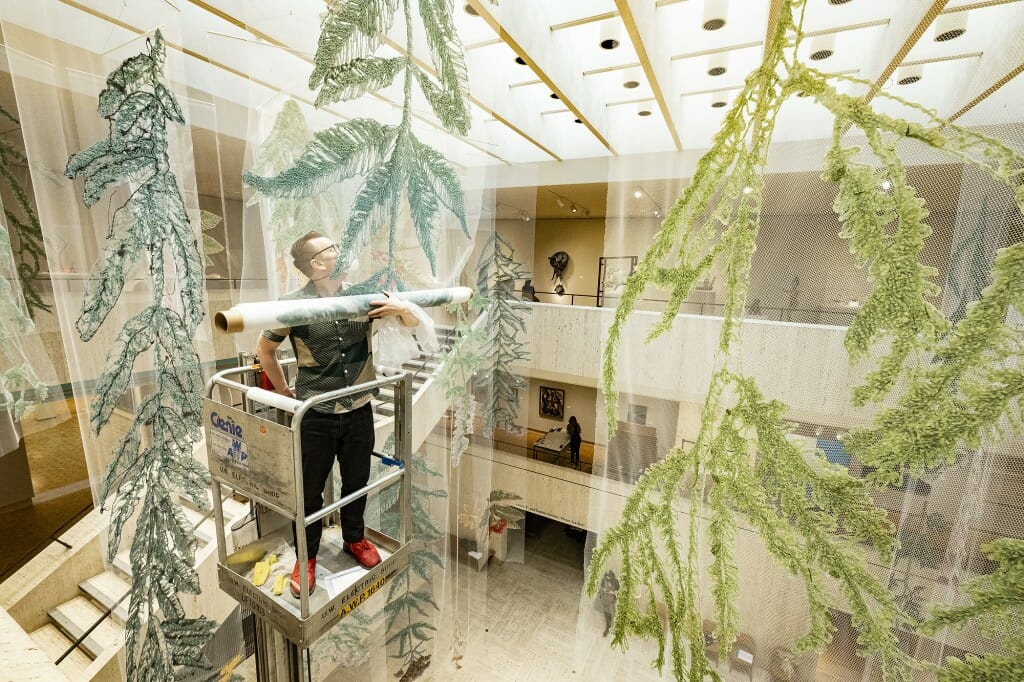 Man on a raised platform hanging large embroidered plants