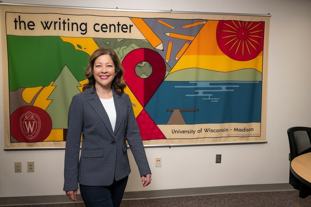 Nancy Linh Karls standing in front of a Writing Center wall hanging