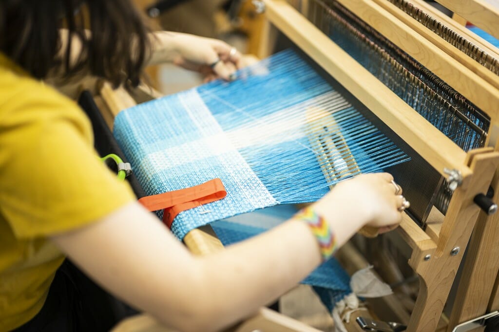 Student Carlyn Kholos works with yarn on a weaving loom.
