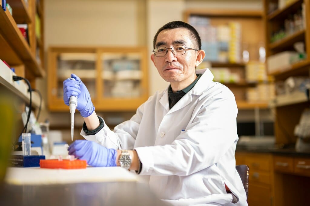 Changjiu Zhao posing in a lab coat and gloves holding a pipette