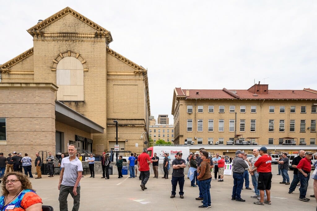 The exterior of a sandstone-colored building, with people crowded outside.