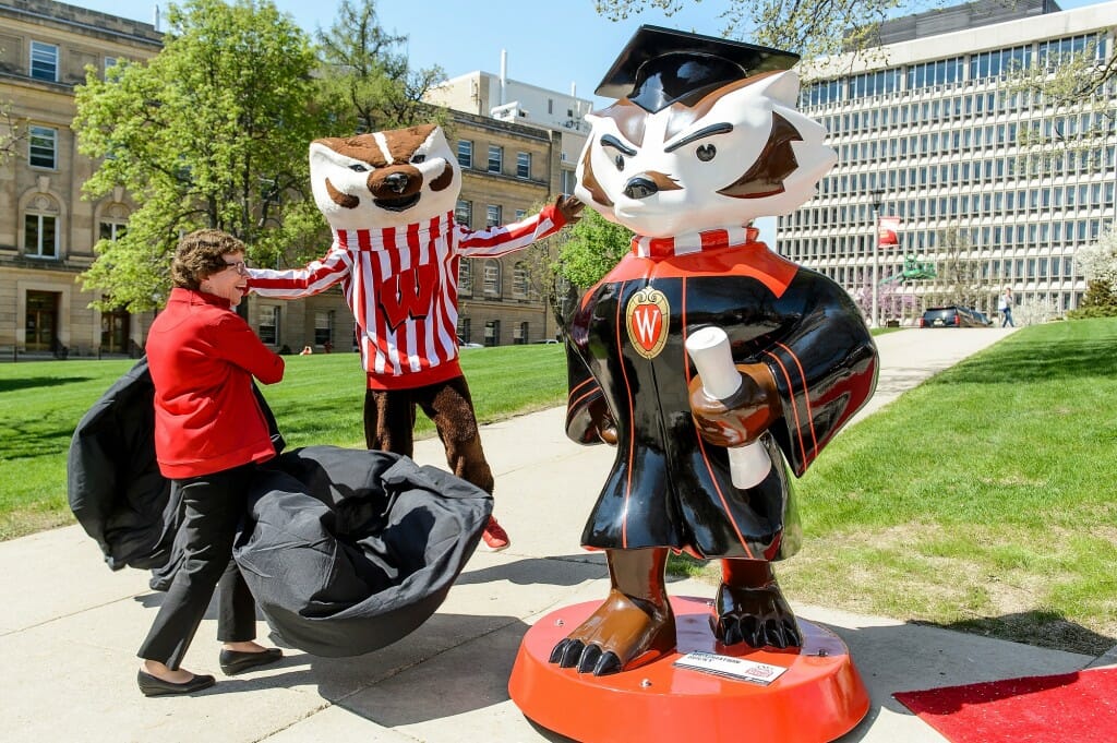 Blank holding a black tarp she just pulled off of a statute while Bucky Badger looks on with arms outstretched