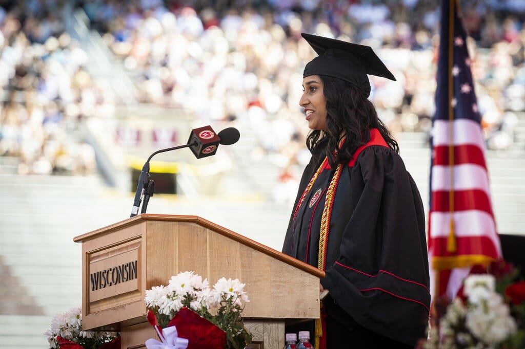 Yahvi, in cap and gown, standing at podium and speaking into microphone