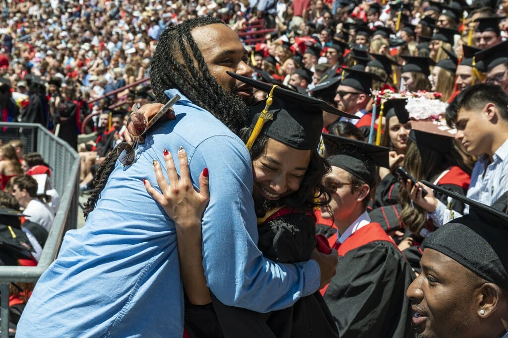 A graduate and another person embracing and smiling in the crowd