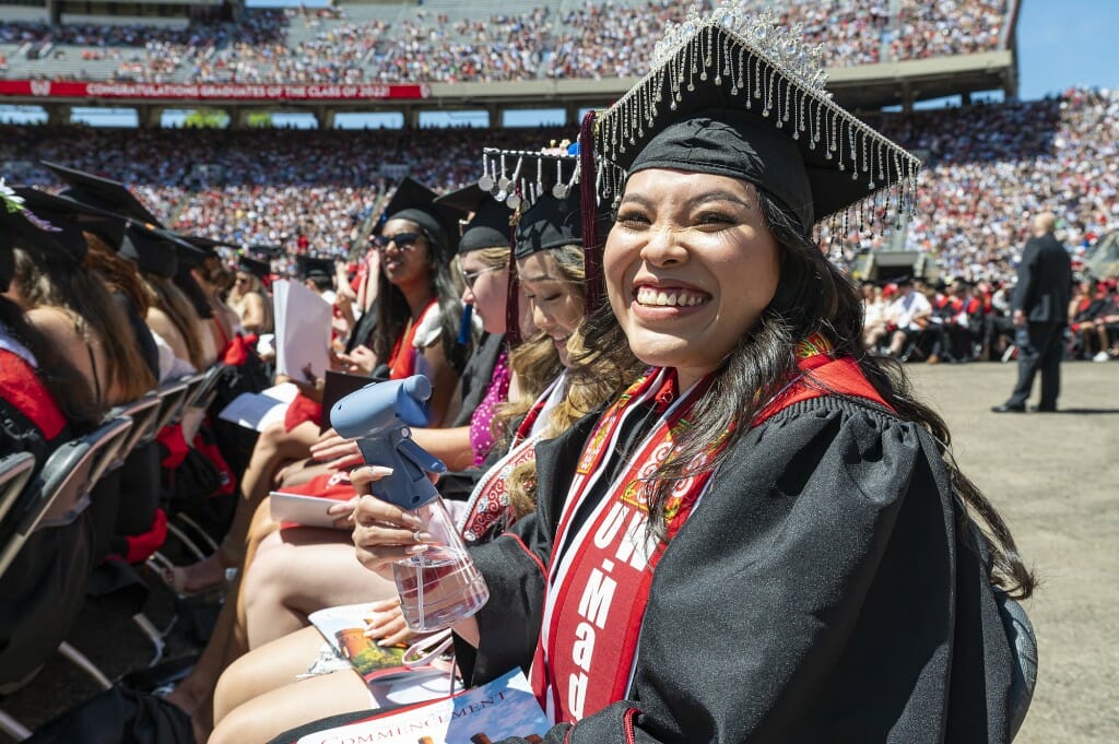 A smiling graduate seated in the back row and looking into the camera