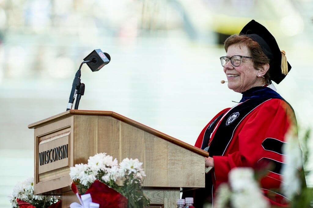 Rebecca Blank wearing academic regalia and smiling while standing at a podium