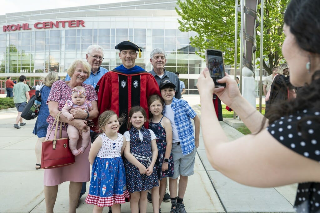 Person in academic robe and hood surrounded by children and adults in his family