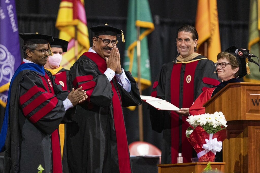 Several people in academic caps and gowns smiling while standing on a stage