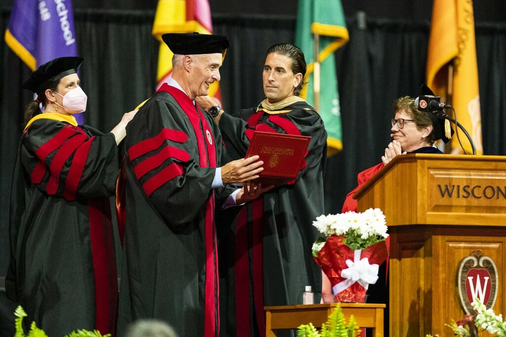 Blank shaking hands with man in academic cap and gown on stage