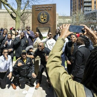Members of Alpha Phi Alpha Fraternity, Inc., celebrate and take photos with their cellphones in front of their fraternity’s plaque.