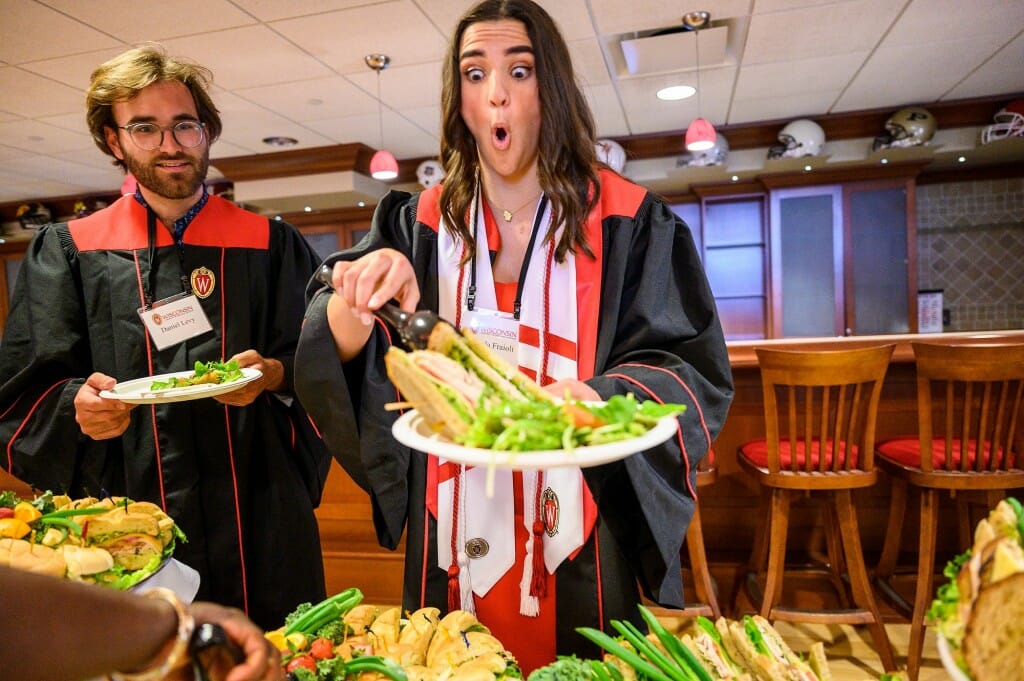 Recent graduate Angela Fraioli appears shocked at the size of the sandwich she is dishing up at the buffet while classmate Daniel Levy looks on.