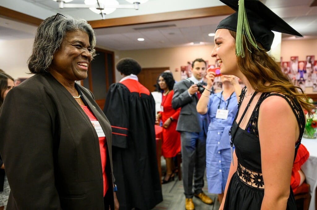 A woman talks with a young woman in a commencement cap as others look on.