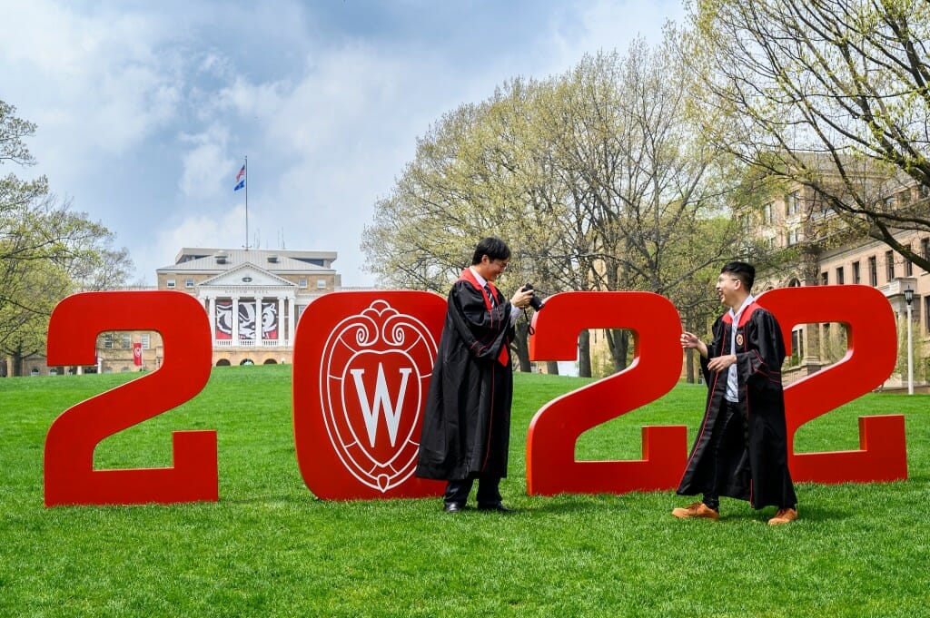 Soon-to-be industrial engineering graduates Dingsheng Tao (left) and Nicholas Tam (right) pose with the numerals “2022” while wearing their graduation gowns on Bascom Hill.