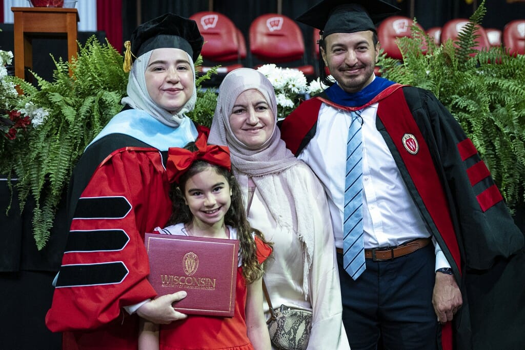 Two people in different cap-and-gown configurations posing with older and younger family members