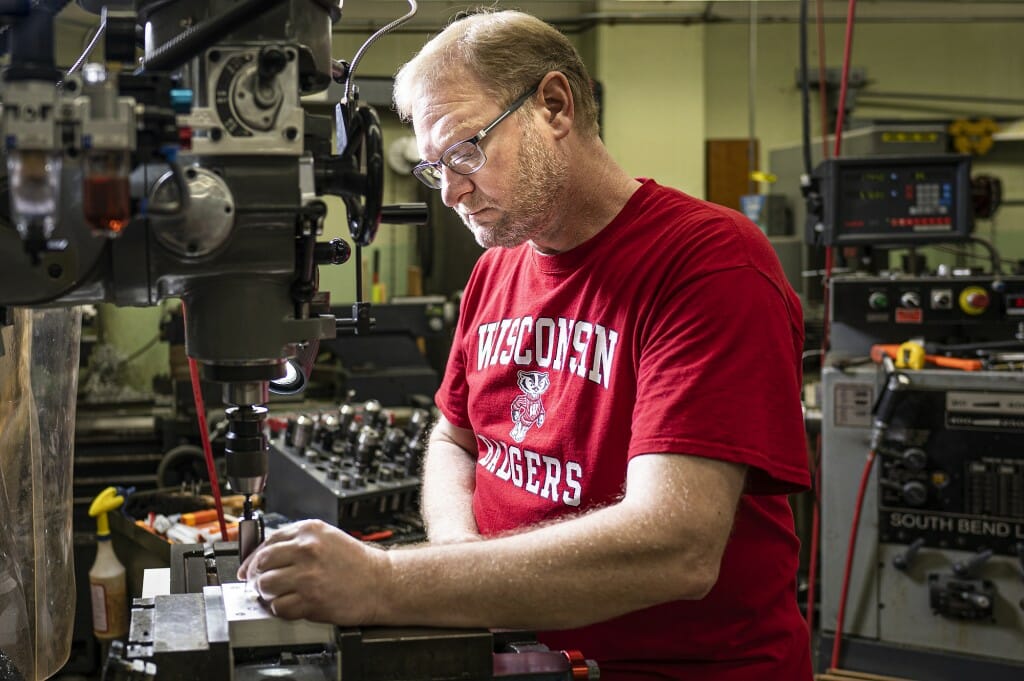 Myers wearing a red Wisconsin T-shirt while working in a machine shop