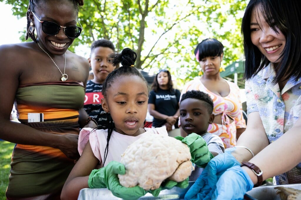 Several fascinated people crowding around a child carefully holding a human brain specimen