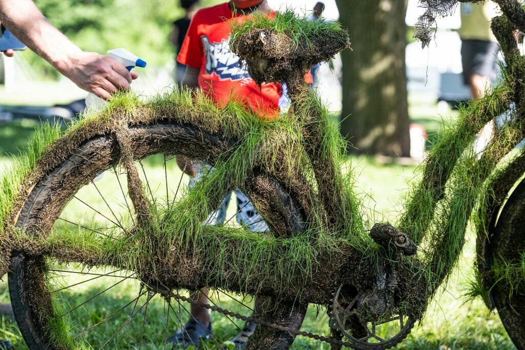 A bicycle with grass growing from its seat, fenders and frame