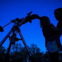 Silhouetted figure leaning toward eyepiece of telescope