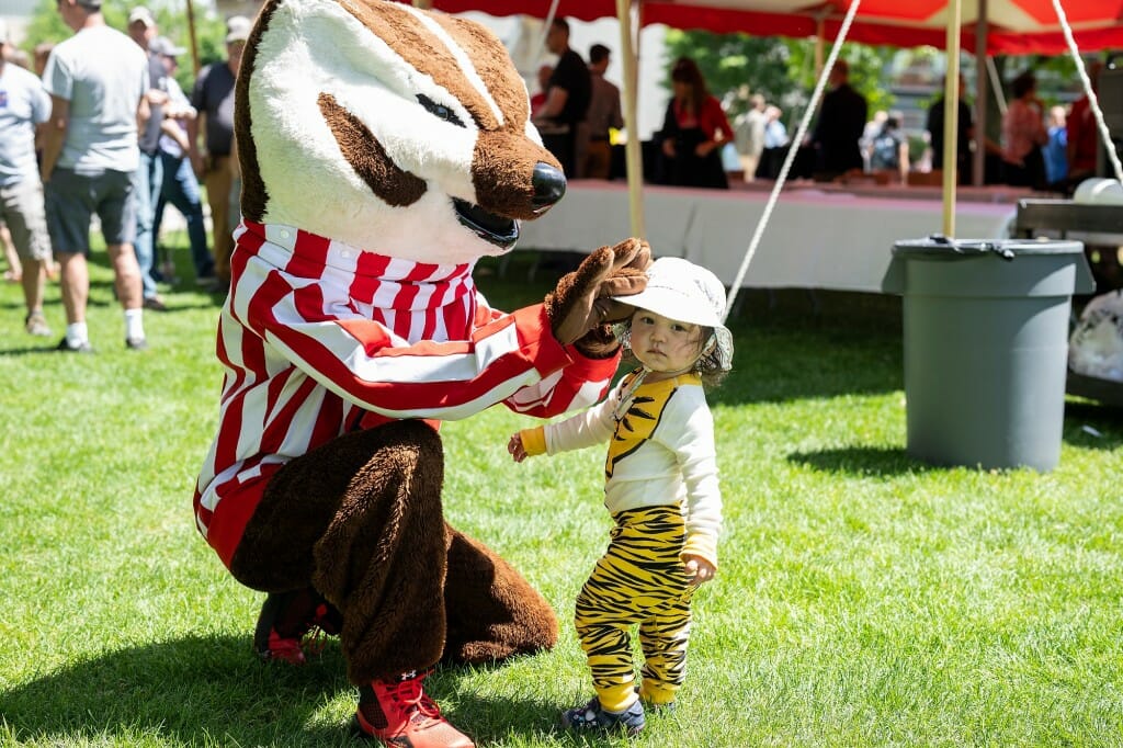 Bucky Badger kneeling next to a small child in a hat