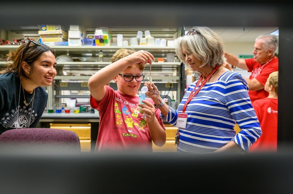 At center, Ian Woods pulls a sample of wheat germ DNA into a test tube held by grandmother Sandy Gilmore, while at left UW student and GPU staff member Luvia Montoya looks on.