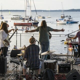 The four band members play music on a lakefront stage.