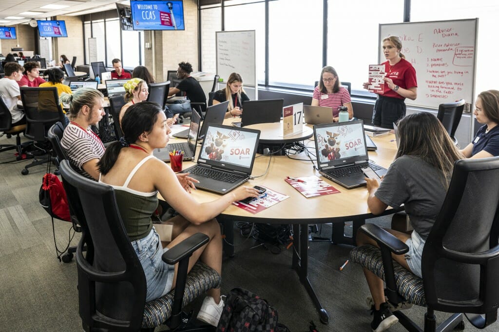 Students sitting around a round table work at laptops.