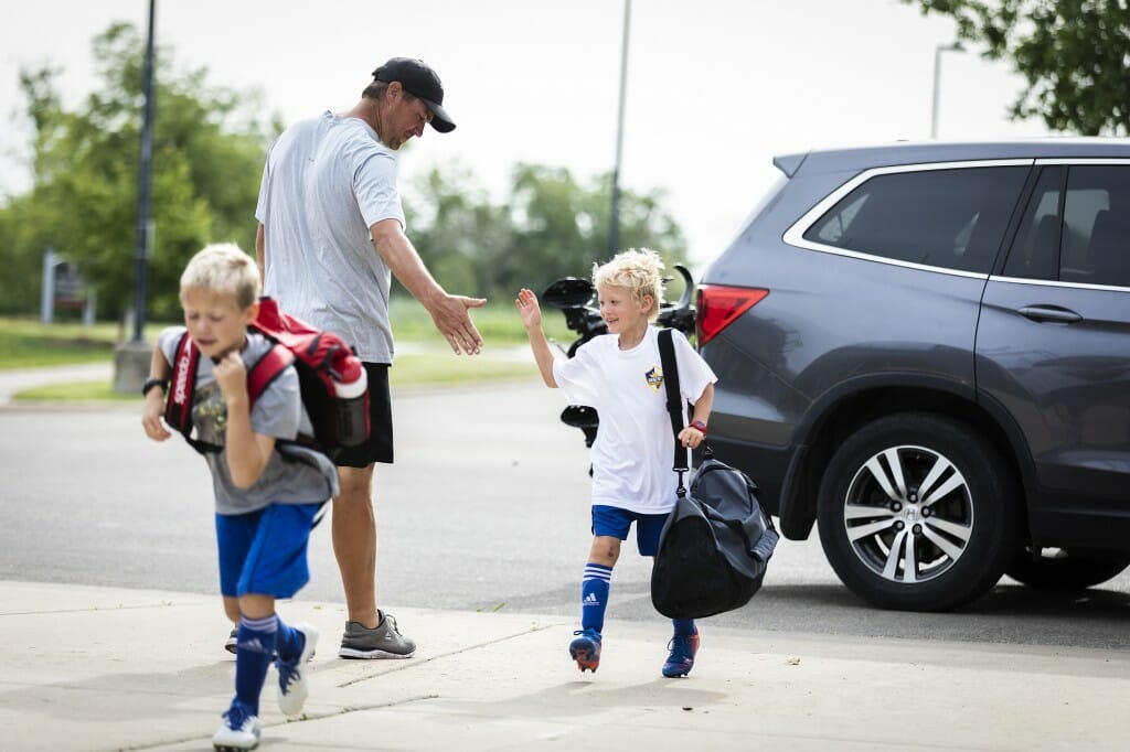 Camp coach Brad Williams greets kids arriving for a UW boys' soccer day camp for ages 4 to 13 at the entrance to Goodman Diamond.