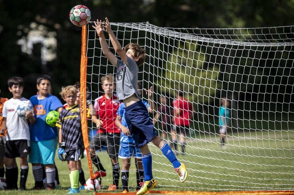 A goalie reaches high for a save at the boys soccer camp.