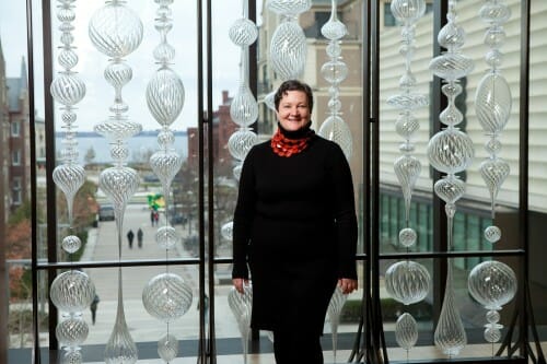 A woman stands in front of a window with glass sculptures in front of it.